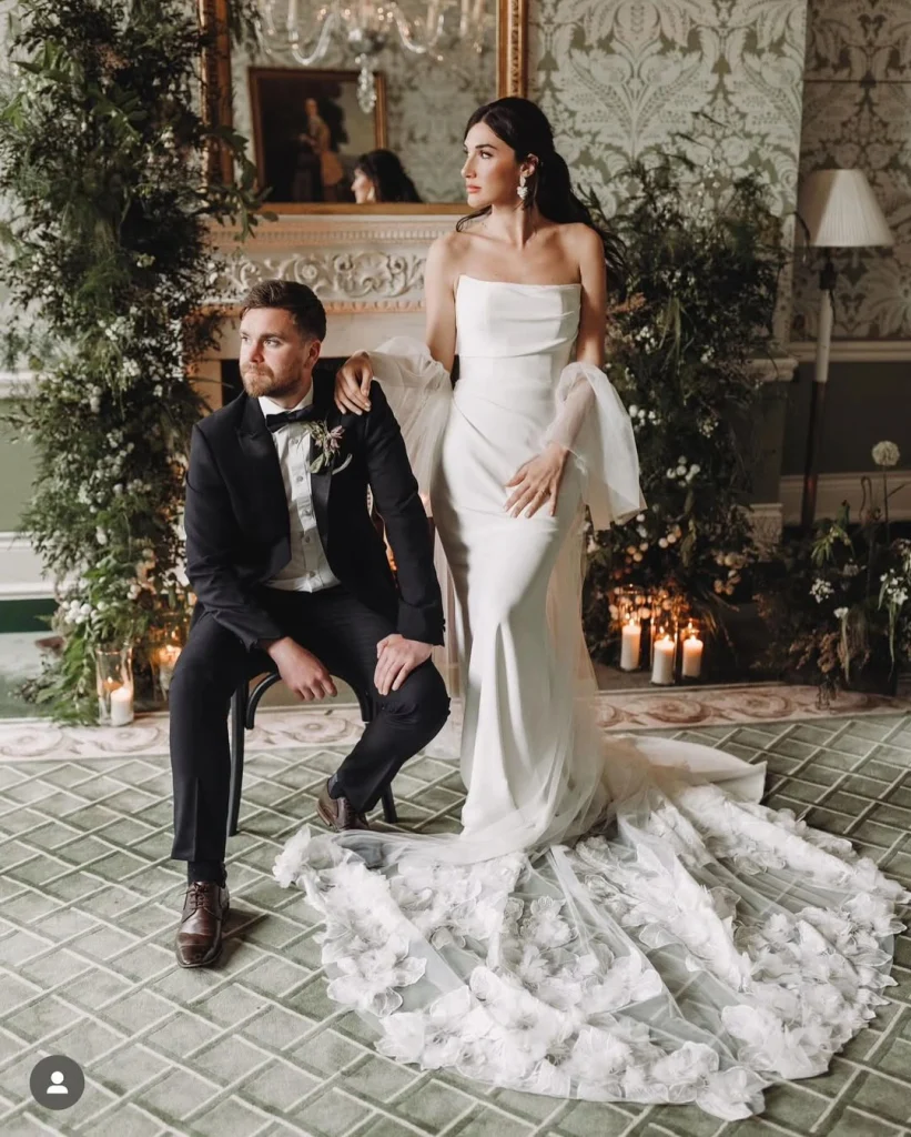 Bride and groom posing; bride in a fitted gown with romantic soft glam makeup.