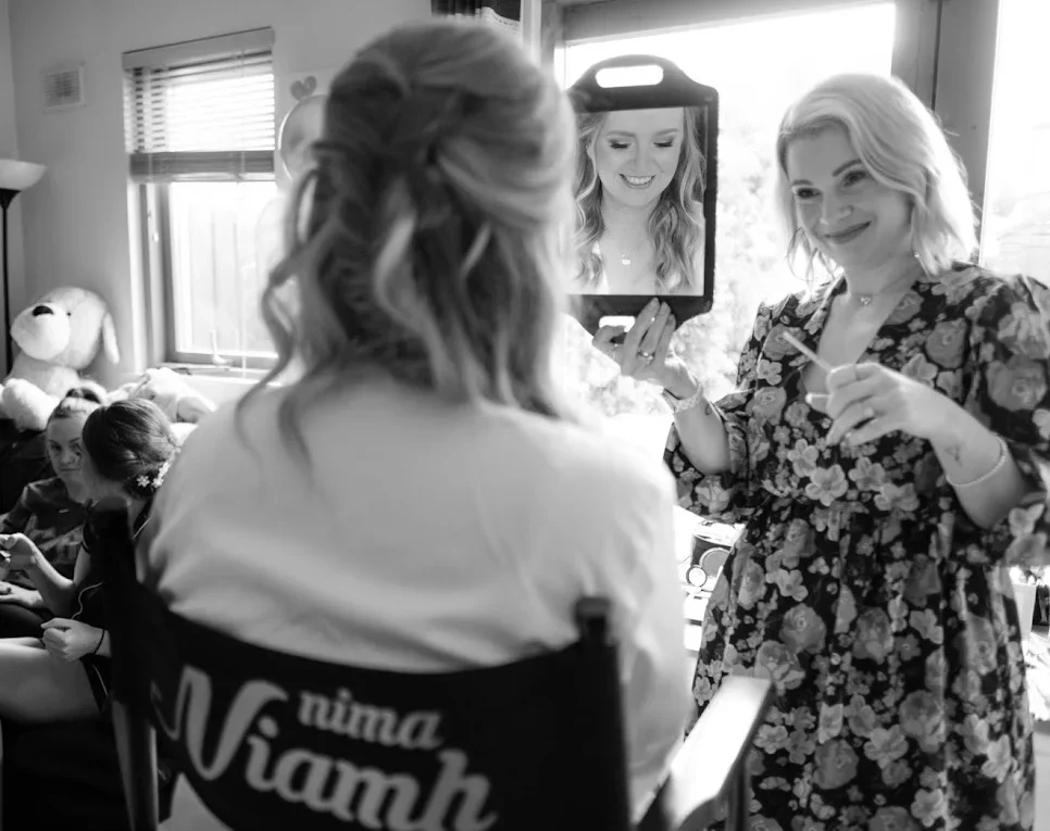Client sitting in makeup artist's Nima's chair as Nima holds up a mirror