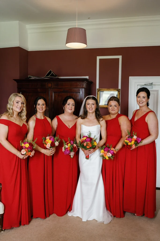 Bride surrounded by her bridesmaids in red dresses - bridal party makeup completed by Nima