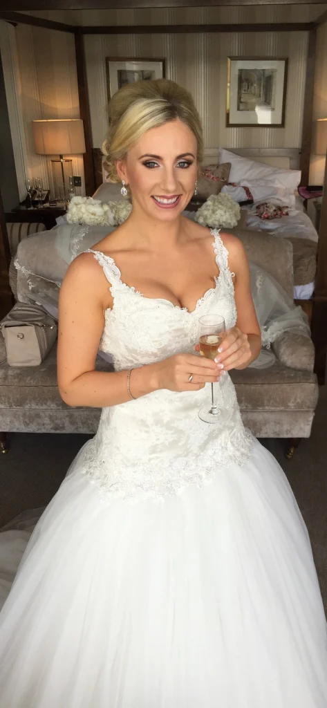 Blonde bride holding a glass of champagne in her dress and finished wedding makeup