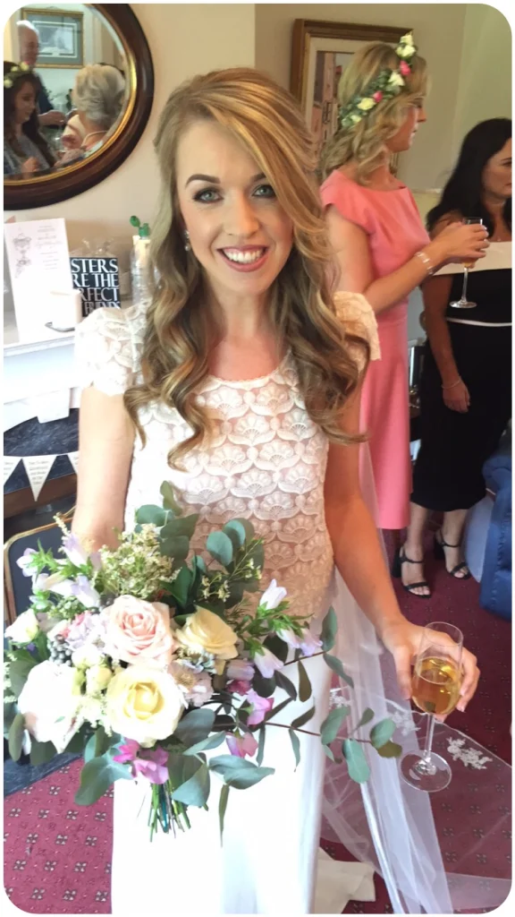Bride holding a glass of champagne and her boquette in her dress and finished wedding makeup