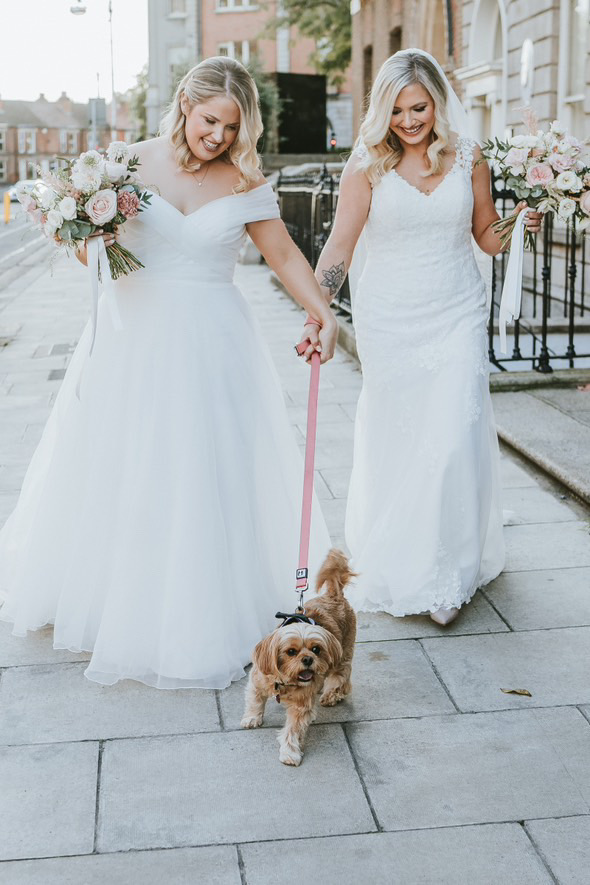 Blonde same-sex brides walking their dog and their flower boquettes - wedding makeup done by Nima