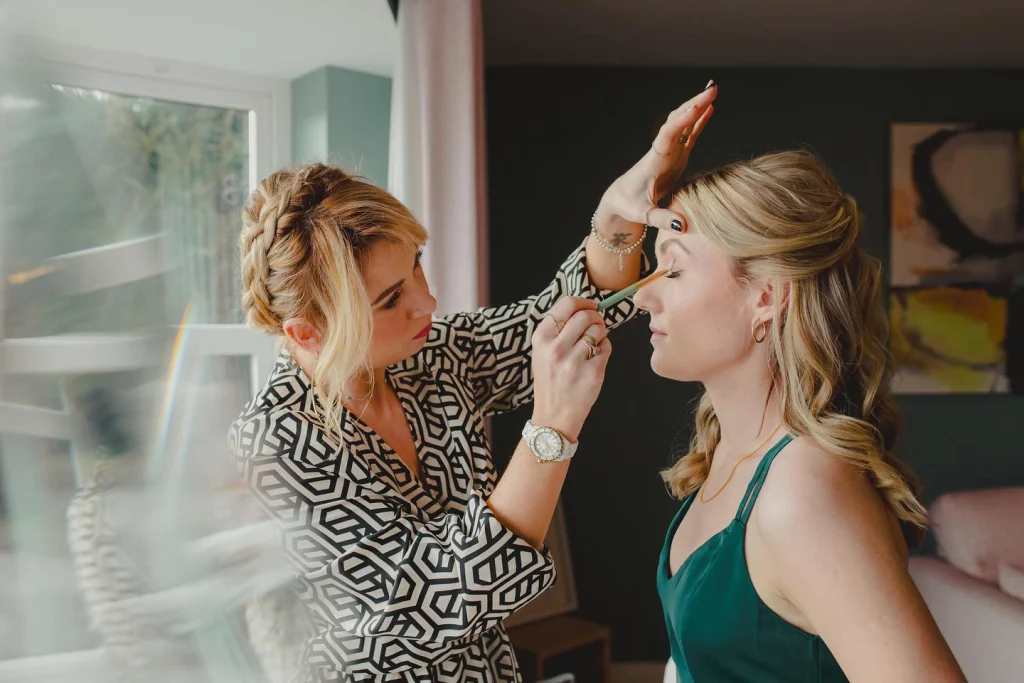 Nima applying wedding makeup on a bridesmaid who's wearing a green dress