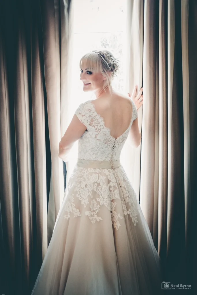 Blonde bride standing in front of curtains with light shinning through